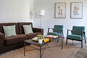 A modern living room with a brown sofa, teal armchairs, a coffee table with a plant, and two framed artworks on the wall. - Barcelona Balconies 12 - Habitat Apartments (Barcelona)