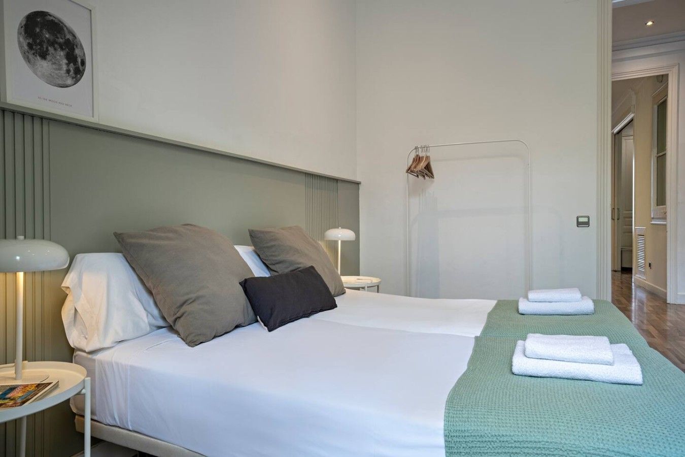 A neatly made bed with pillows, a bedside lamp, and a green blanket on the floor.