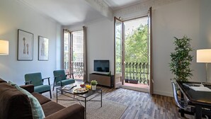 A modern living room with a sofa, chairs, a coffee table, a TV, and a balcony with a view of greenery. - Barcelona Balconies 12 - Habitat Apartments (Barcelona)