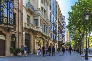 A historic street with ornate architecture, including a building with a large arched entrance and a sign that reads "LECOA". - Barcelona Balconies 12 - Habitat Apartments (Barcelona)