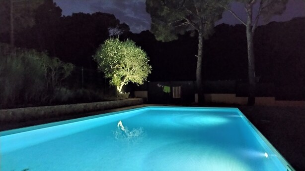 A rectangular swimming pool with a clear blue water surface, surrounded by a dark, landscaped area with trees and a fence. - Superb Villa 8-10 persons with private pool, near beach (Pals)