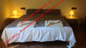 A neatly made bed with white linens and two towels folded on it, two bedside lamps, and a plain wall in the background. - Superb Villa 8-10 persons with private pool, near beach (Pals)