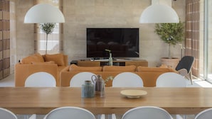 Ein modernes Wohnzimmer mit einer Sofagarnitur, einem Esstisch und einem Fernseher.