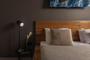 A neatly made bed with white linens and a wooden headboard, a bedside lamp, and a small table with a vase of flowers.