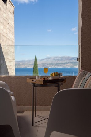 A balcony with a table set for two, a glass of orange juice, and a bowl of fruit. - Villa Ana — Private Sea Ray 230 SPX OB Yacht & Mercedes V-Class with Driver (Splitska)