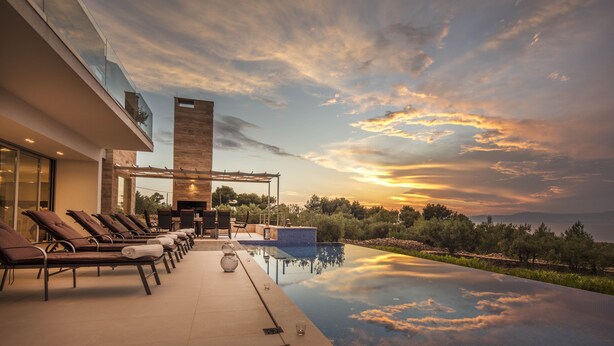 Ein Pool ohne Ende mit Blick auf den Sonnenuntergang, Liegestühle und ein Kamin.