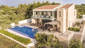 Ein modernes, zweistöckiges Haus mit Swimmingpool, Sitzgelegenheit im Freien und Blick auf die umliegende Grünfläche.