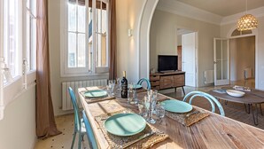 A dining area with a wooden table set for four, a television in the background, and a view of the outside through a window. - Bailén Style - Habitat Apartments (Barcelona)