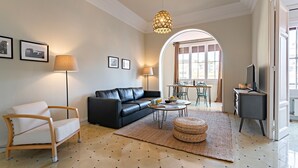 A living room with a sofa, armchair, coffee table, and a TV stand. - Bailén Style - Habitat Apartments (Barcelona)