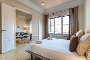 A hotel room with a large bed, a sitting area with a sofa and table, and a window with curtains.