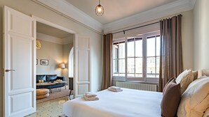 A hotel room with a large bed, a sitting area with a sofa and table, and a window with curtains. - Bailén Style - Habitat Apartments (Barcelona)