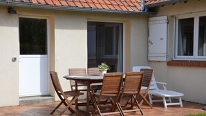 Un patio con una mesa y sillas de madera, una planta en maceta y un sillón blanco.