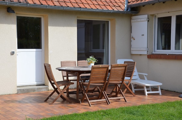 A patio with a wooden table and chairs, a potted plant, and a white lounge chair.