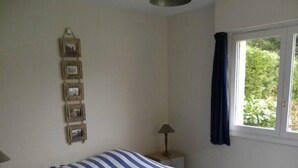 Un dormitorio con cama, mesita de noche, lámpara, ventana con cortinas y cuadros enmarcados en la pared.