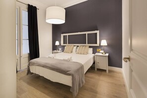 A hotel room with a bed, two bedside tables, a large window, and a hanging light fixture.