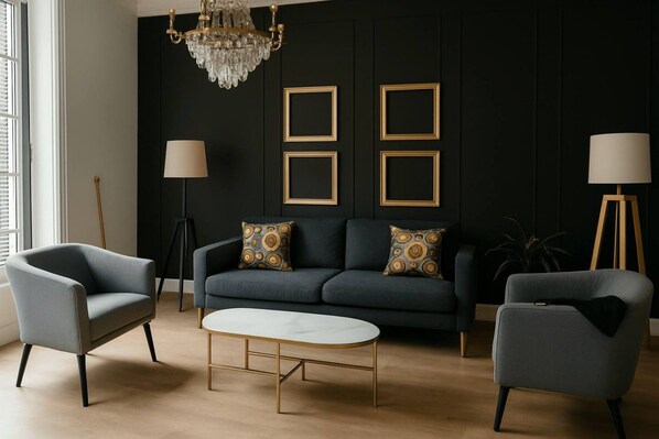 A modern living room with a dark wall, a chandelier, a sofa with patterned cushions, two armchairs, a coffee table, and floor lamps.
