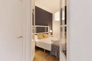 A hotel room with a bed, bedside table, lamp, and a view through a glass door. - Grace 1 - Habitat Apartments (Barcelona)