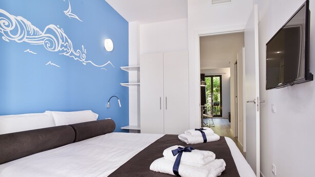 A modern hotel room with a large bed, a blue wall mural, a TV, and a view into the bathroom.