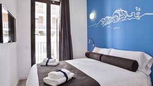A hotel room with a bed, a TV, a window with curtains, and a wall with a blue design.