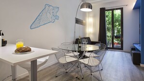 A modern dining area with a white table, metal wire chairs, and a glass top. There is a bottle of wine, a glass, and a plate with food on the table.