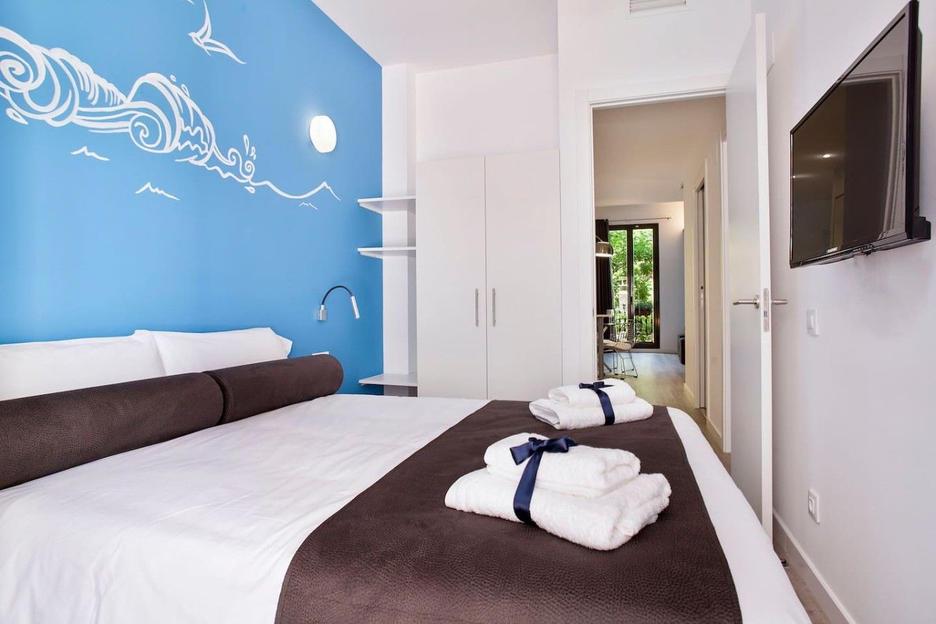 Une chambre d’hôtel avec un lit, une fresque murale bleue, un téléviseur et une vue sur l’extérieur.