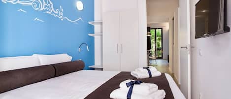 A hotel room with a bed, a blue wall mural, a TV, and a view of the outdoors.