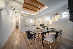 Une cuisine moderne avec des meubles blancs, un îlot central et un coin repas comprenant une table et des chaises en bois.