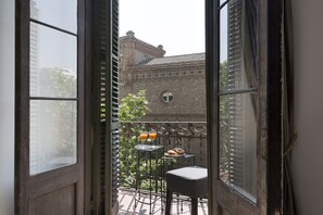 A balcony with a table and chairs, a railing, and a view of a building with a tiled roof. - Grace 2 - Habitat Apartments (Barcelona)