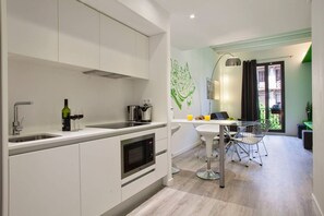 A modern kitchen with a built-in oven, a dining area with a table and chairs, and a view of the outside through a window. - Chic Sants Gem ADN 21 (Barcelona)