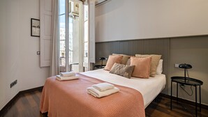 A neatly made bed with a patterned bedspread and pillows, a bedside table with a lamp, and a window with curtains.