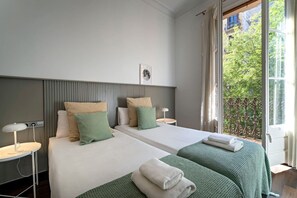 Hotellihuone, jossa on kaksi sänkyä, yöpöytä lampun kanssa, ikkuna, josta on näkymä vehreään maisemaan, ja ovi.