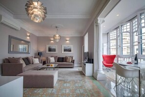 A modern living room with a sectional sofa, a coffee table, and a red chair. There are two wall-mounted televisions and a dining area with a table and chairs. - Huge Eixample Luxury Flat Barcelona Classic (Barcelona)