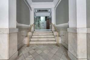 A marble staircase with a handrail, leading to a door with a glass panel.