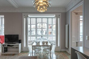 A dining area with a table set for six, a television on a stand, and a large window with a view of buildings. - Huge Eixample Luxury Flat Barcelona Classic (Barcelona)