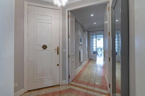A hallway with a white door, a patterned rug, and a view into another room.