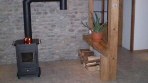Ein rustikaler Raum mit einer Steinwand, einem kleinen Holzofen, einem hölzernen Regal mit einer Topfpflanze und einer Tür zu einem anderen Raum.