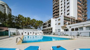 A swimming pool with two blue lounge chairs, surrounded by modern buildings and trees. - Cascais Panoramic with Pool by Portugal Portfolio (Cascais)