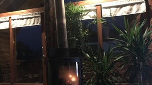 Un poêle à bois installé dans un espace extérieur accueillant, avec des portes en bois et des plantes en pot.