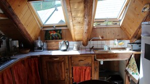 Une cuisine de taille réduite, avec des meubles de rangement en bois, un évier et une fenêtre au-dessus du plan de travail.