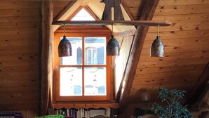 Un intérieur rustique avec des éléments en bois, un plafond en pente, une fenêtre en bois offrant une vue et trois lampes suspendues.