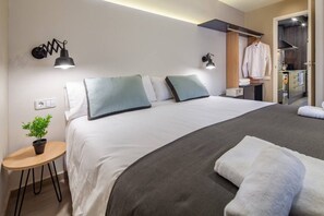 Une chambre d’hôtel moderne avec un grand lit, des lampes de chevet, une petite table avec une plante et un dressing avec un portant à vêtements.