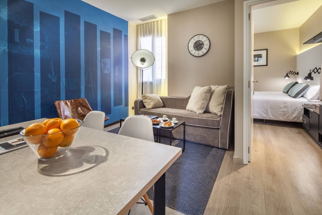 Et moderne hotelværelse med spiseplads, en sofa, en seng og et ur på væggen.