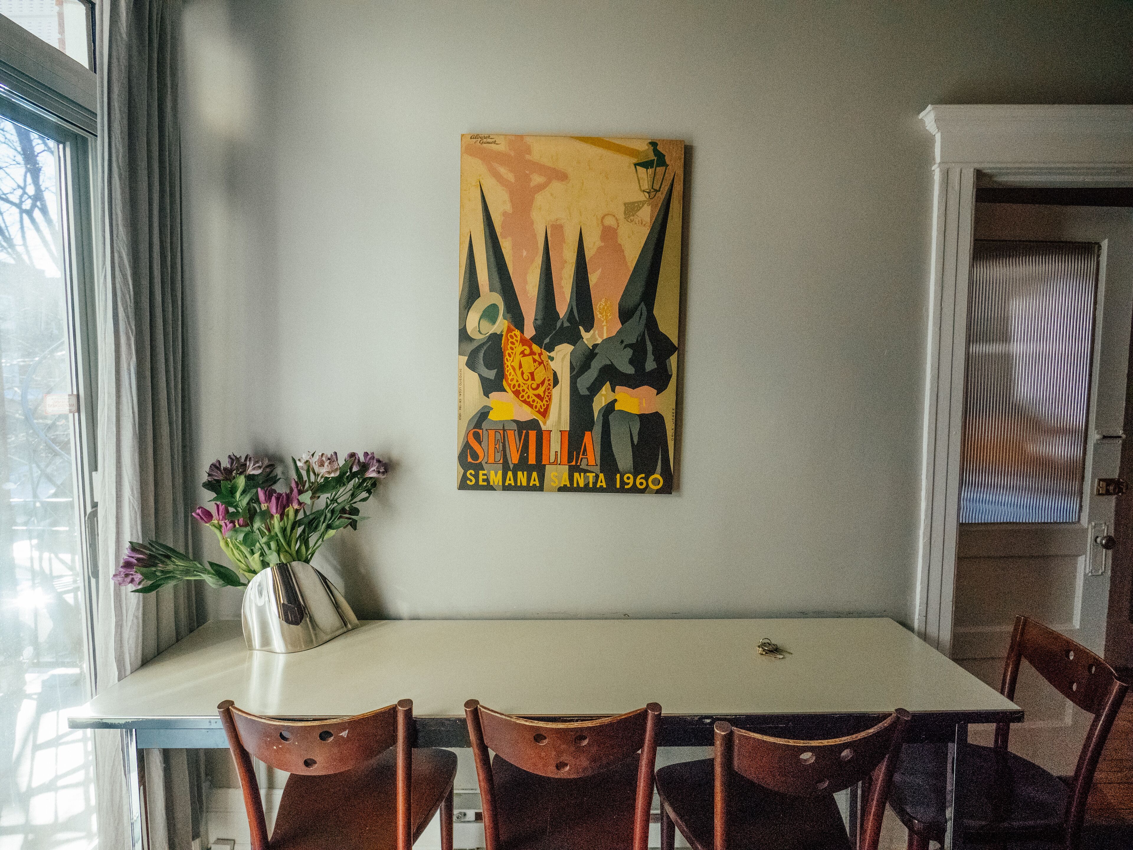 A dining area with a table, chairs, a vase with flowers, and a poster on the wall.