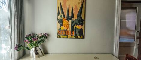 A dining area with a table, chairs, a vase with flowers, and a poster on the wall.