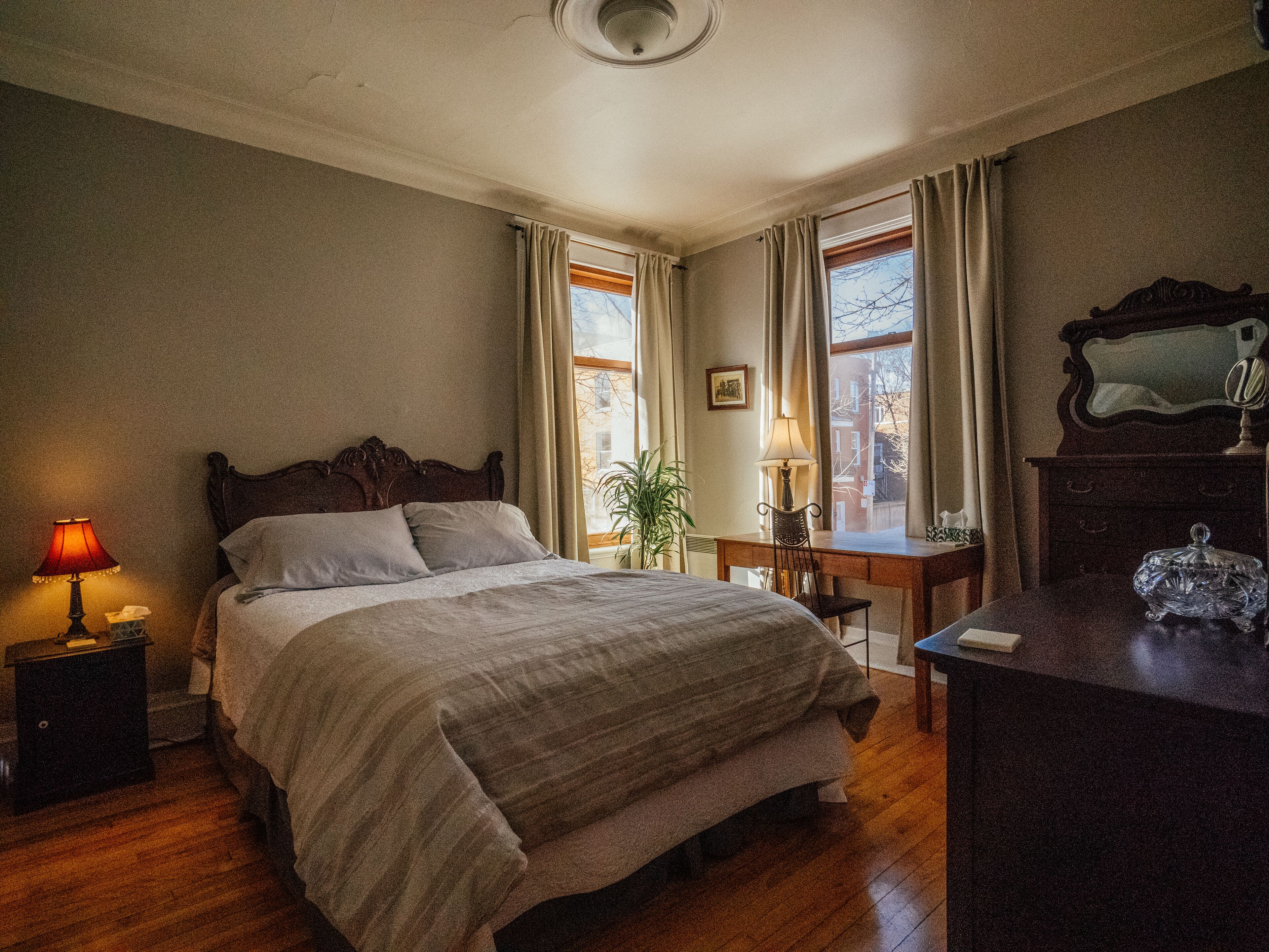 Un dormitorio con una cama grande, un escritorio, un aparador y una ventana con cortinas.