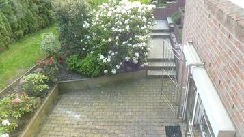 Eine Backstiege führt zu einem Hauseingang, umgeben von Grünpflanzen und Blumen.