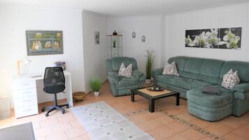 Ein Wohnzimmer mit Schreibtisch, zwei grünen Sofas, einem Couchtisch und Wanddekoration.