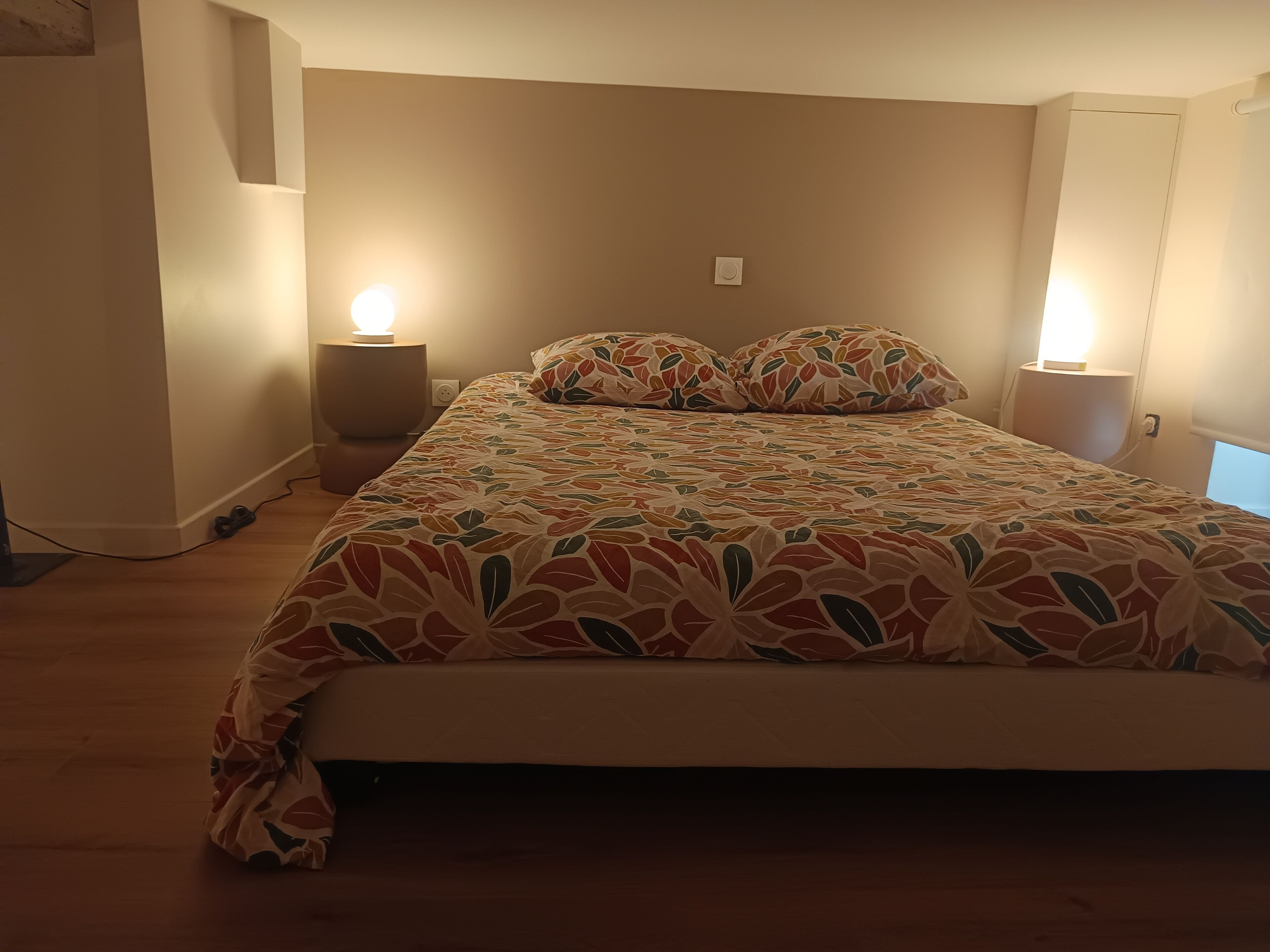A bedroom with a bed, two bedside lamps, and a wall-mounted thermostat.