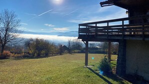 Uma estrutura de madeira com varanda, com vista para um campo gramado e céu claro.