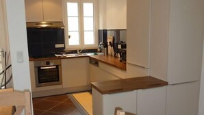 Une cuisine compacte équipée d’un four encastré, d’un four à micro-ondes et d’un évier. On y trouve une chaise en bois et une petite table à manger.